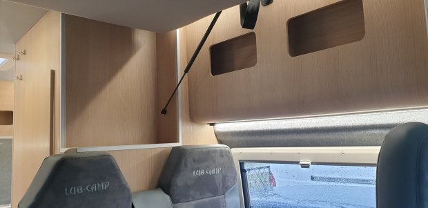 Wnętrze kampera: drewniane szafki, podniesiony schowek i fotele z napisem LUB-CAMP.