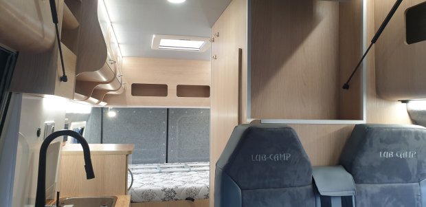 Wnętrze kampera z drewnianymi szafkami, fotelem LUB-CAMP i łóżkiem w tyle