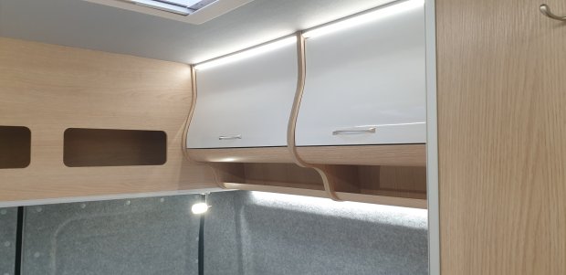 Górne szafki z jasnego drewna i białymi frontami oraz wąskim oświetleniem LED