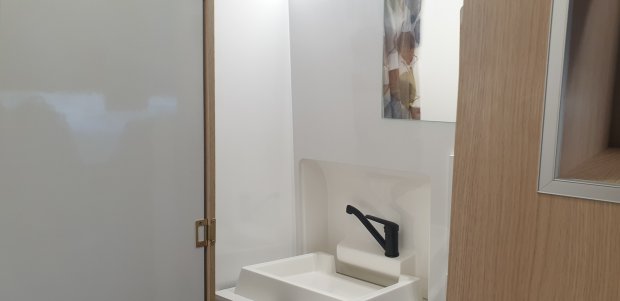 Mała biała umywalka z czarną baterią w kompaktowej łazience, drewniane drzwi i lustro