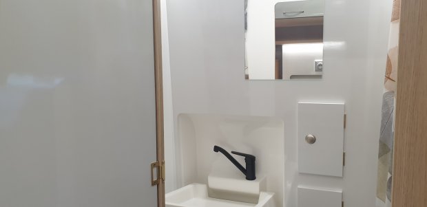 Mała umywalka z czarną baterią, lustrem i szafką w jasnej kabinie