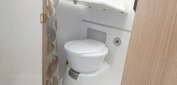 Mała biała toaleta kasetowa w kompaktowej łazience z zasłoną w liście