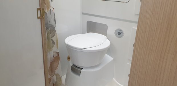 Mała toaleta kasetowa w łazience kampera, zasłona w liście i drewniane drzwi