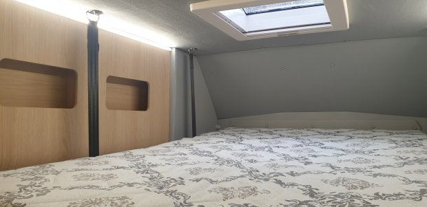 Łóżko w kamperze z wzorzystym materacem, drewnianą ścianą i oknem dachowym