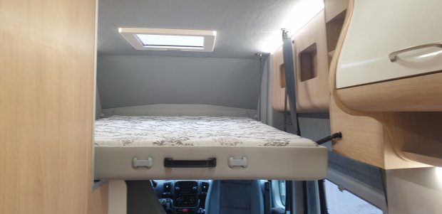 Łóżko nad kabiną kampera z oknem dachowym i drewnianymi szafkami