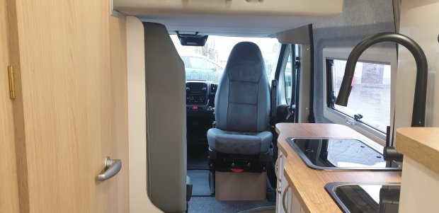 Wnętrze kampera z fotelem kierowcy, blatem kuchennym, zlewem i oknem.