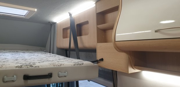 Górne łóżko w kamperze z materacem, pasami zabezpieczającymi i drewnianymi półkami