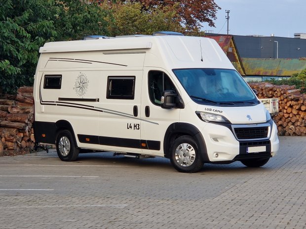 Biały kamper zaparkowany obok stosu pociętego drewna