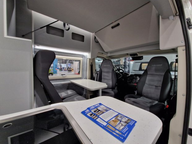 Wnętrze kampera: obrotowe fotele, stół, blat kuchenny i opuszczane łóżko.