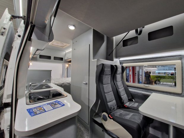 Wnętrze kampera z aneksem kuchennym, dwoma fotelami i stołem
