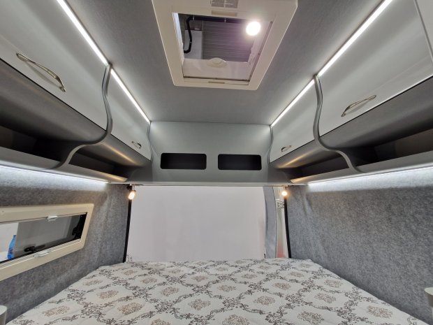 Sypialnia kampera z łóżkiem, górnymi szafkami i świetlikiem w suficie