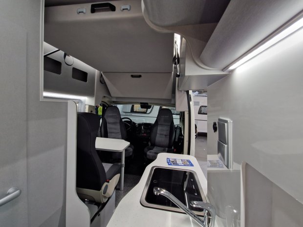 Wnętrze kampera: kuchnia ze zlewem, stolik i obrotowe fotele kierowcy i pasażera