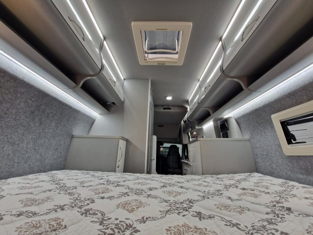 Wnętrze kampera z łóżkiem, podświetlonymi półkami i oknem dachowym