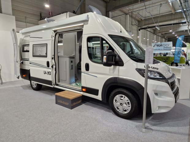 Biały kamper z otwartymi drzwiami, wystawiony na targach
