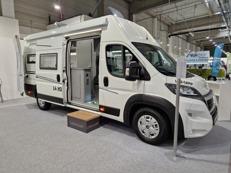 Biały kamper z otwartymi drzwiami, wystawiony na targach