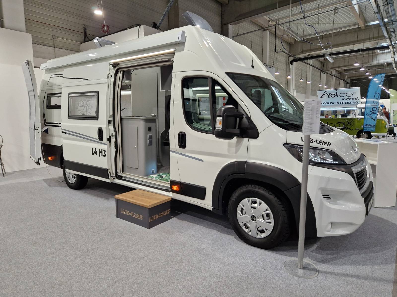 Biały kamper z otwartymi drzwiami, wystawiony na targach