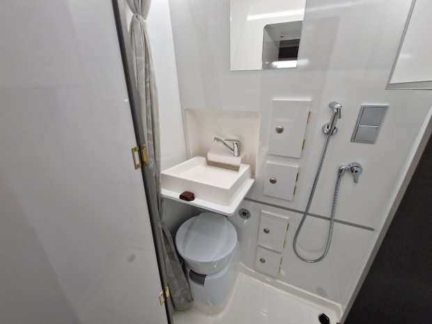 Mała biała łazienka kempingowa z umywalką, toaletą, prysznicem i schowkami
