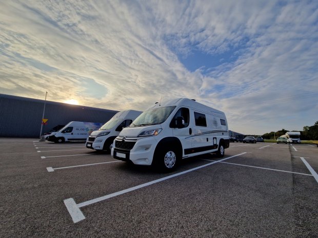 Białe kampery zaparkowane na dużym parkingu pod rozległym zachmurzonym niebem