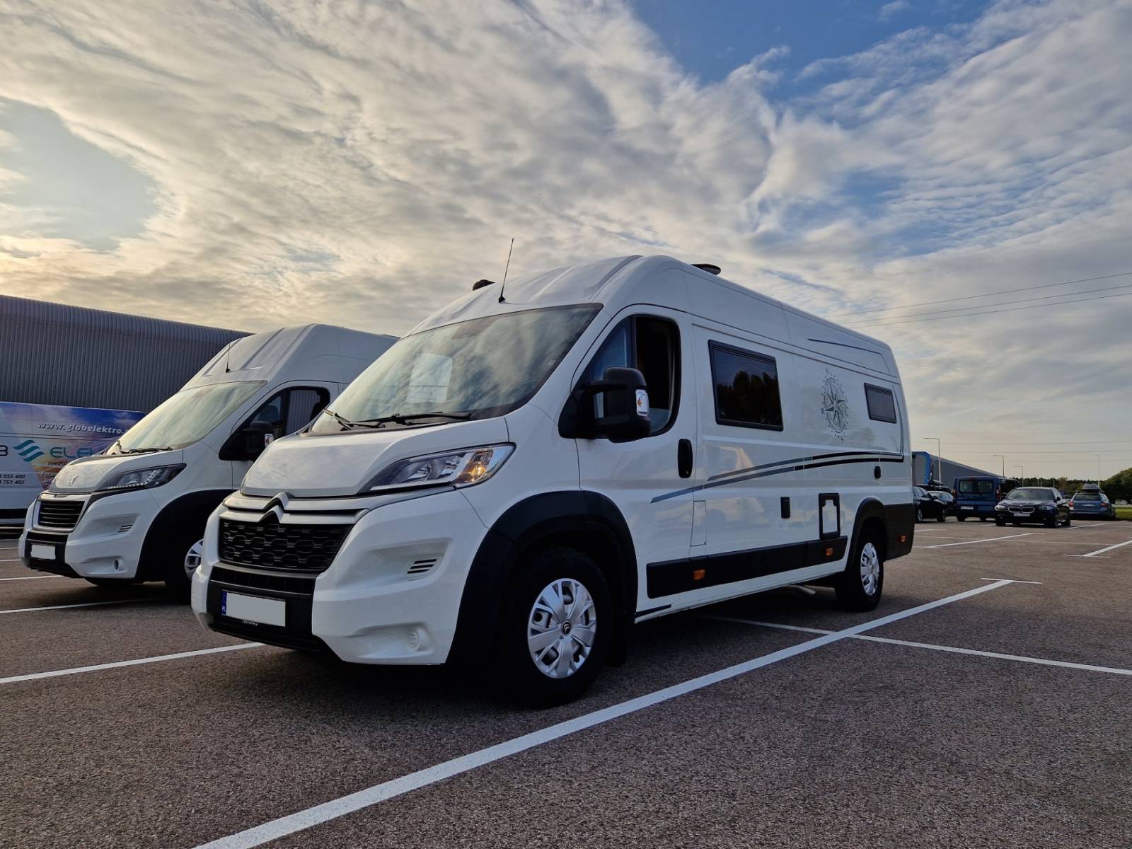 Biały kamper zaparkowany na parkingu obok podobnego pojazdu pod chmurnym niebem