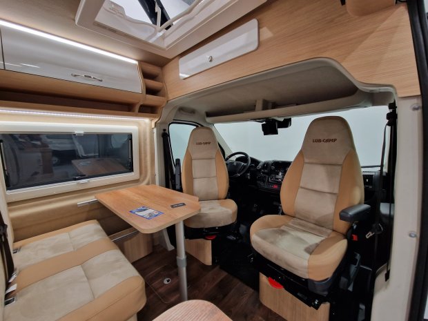 Wnętrze kampera z obrotowymi fotelami, stołem i drewnianymi szafkami