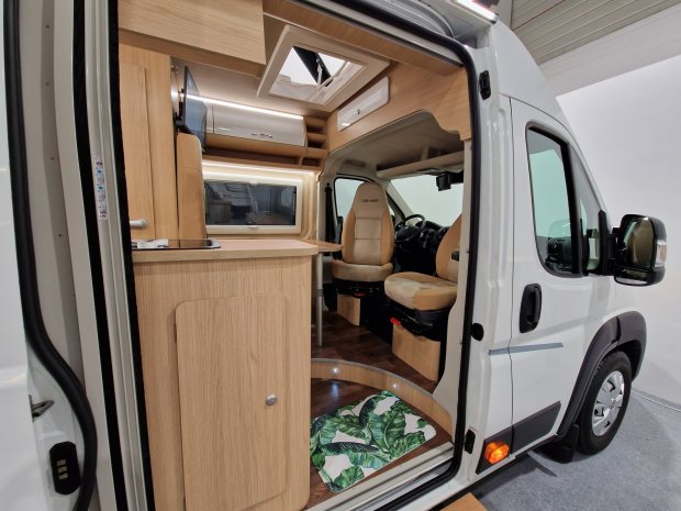 Wnętrze kampera: jasne drewno, obrotowe fotele kierowcy i pasażera, mała kuchnia