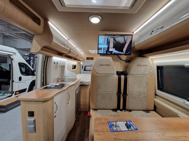 Wnętrze kampera z aneksem kuchennym, siedzeniami LUB-CAMP i telewizorem.