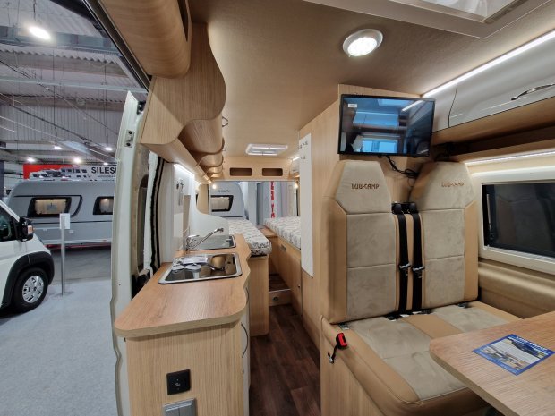 Wnętrze kampera: drewniany aneks kuchenny, siedzenia z pasami i tylne łóżko.