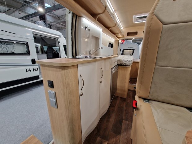Wnętrze kampera z jasnym aneksem kuchennym, zlewem i tapicerowanym siedzeniem