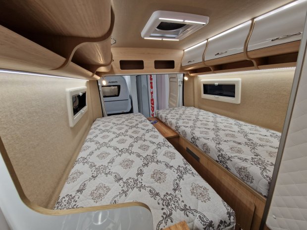 Wnętrze kampera z dwoma oddzielnymi łóżkami, szafkami i oknami.