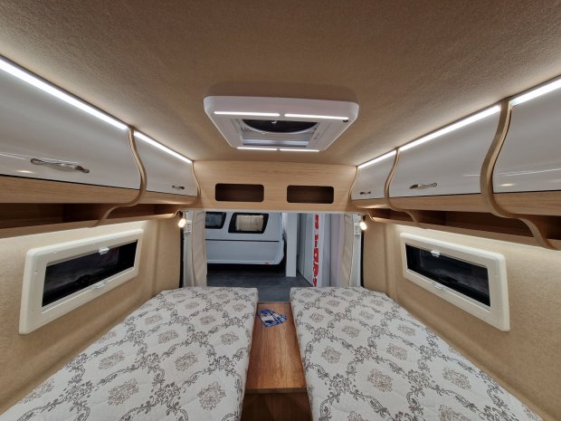 Wnętrze kampera: dwa łóżka, górne szafki, boczne okna i świetlik