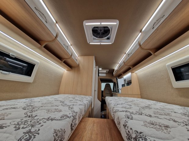 Wnętrze kampera: dwa łóżka, drewniane szafki, oświetlenie LED i wentylator sufitowy