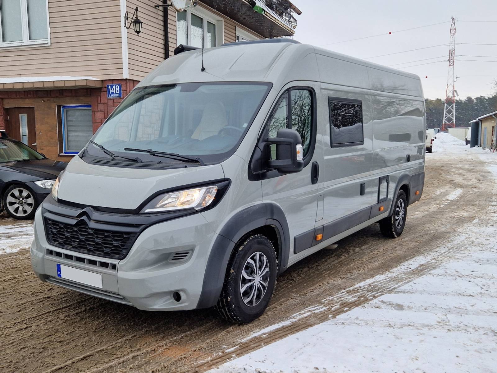 Szary kamper zaparkowany na zaśnieżonej, błotnistej ulicy obok domów