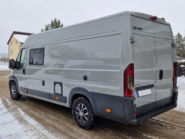 Szary van kamper zaparkowany na zaśnieżonej drodze, widok z tyłu i boku.