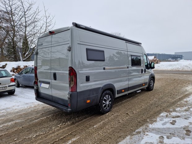 Szary kamper zaparkowany na zaśnieżonej, błotnistej drodze, widok z tyłu i boku