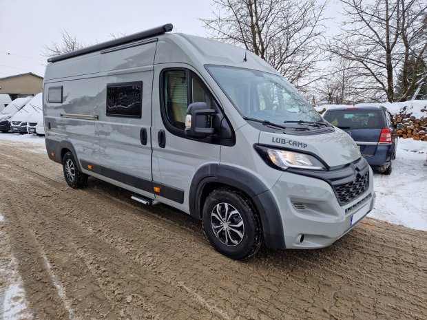 Srebrny kamper typu bus zaparkowany na zaśnieżonej, błotnistej drodze.