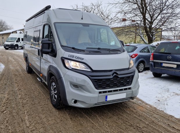 Szary kamper LUB-CAMP zaparkowany na zaśnieżonej, błotnistej drodze między autami.