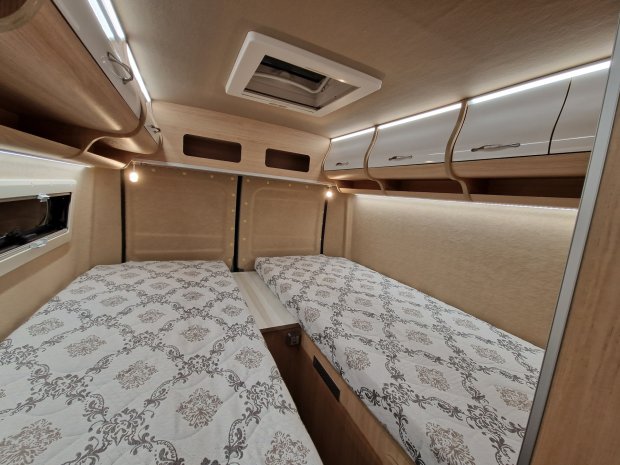 Wnętrze kampera: dwa pojedyncze łóżka, górne szafki, oświetlenie i świetlik.