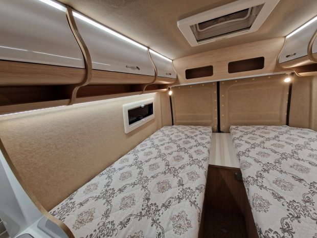 Wnętrze kampera z dwoma pojedynczymi łóżkami, szafkami i oświetleniem LED.