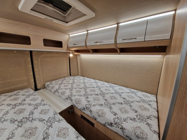 Wnętrze kampera: dwa pojedyncze łóżka, górne szafki z podświetleniem i drewniane panele