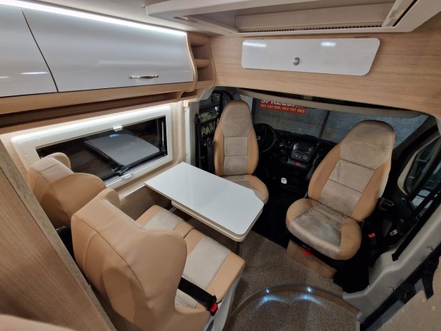 Wnętrze kampera: stół, obrotowe fotele kierowcy i pasażera oraz tapicerowane siedzenia.