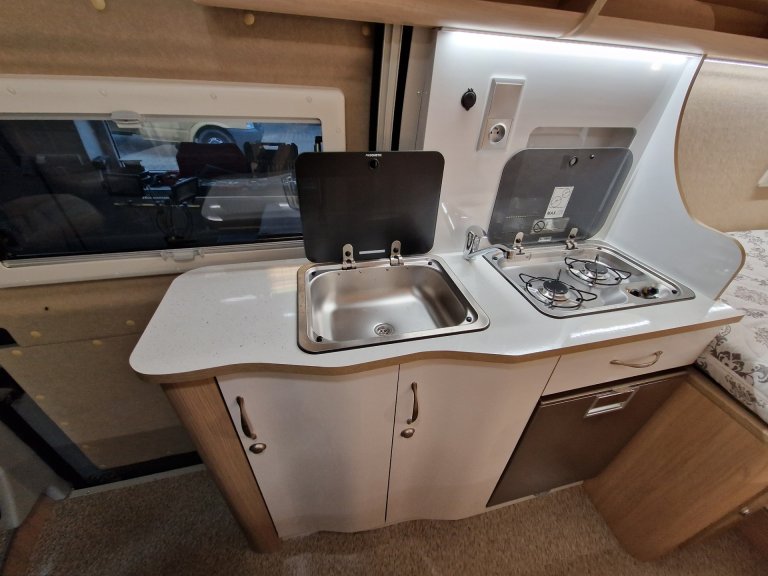 Kompaktowa kuchnia w kamperze z zlewem, dwiema kuchenkami i szafkami.