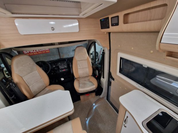 Wnętrze kampera z obrotowymi fotelami kierowcy, stolikiem i kuchnią.