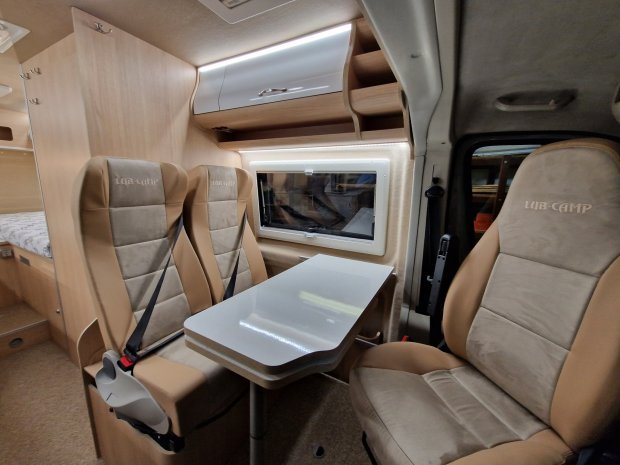 Wnętrze kampera z stołem i trzema beżowymi fotelami z napisem LUB-CAMP