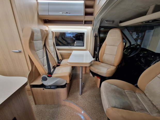 Wnętrze kampera z białym stolikiem i czterema beżowymi fotelami.