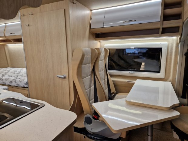 Wnętrze kampera z dwoma beżowymi fotelami, składanym stolikiem i kuchennym blatem.