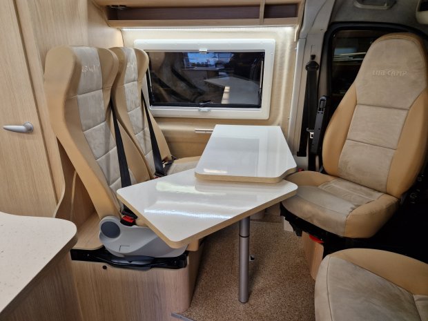 Wnętrze kampera: dwa obrócone fotele i wysuwany składany stolik przy oknie.