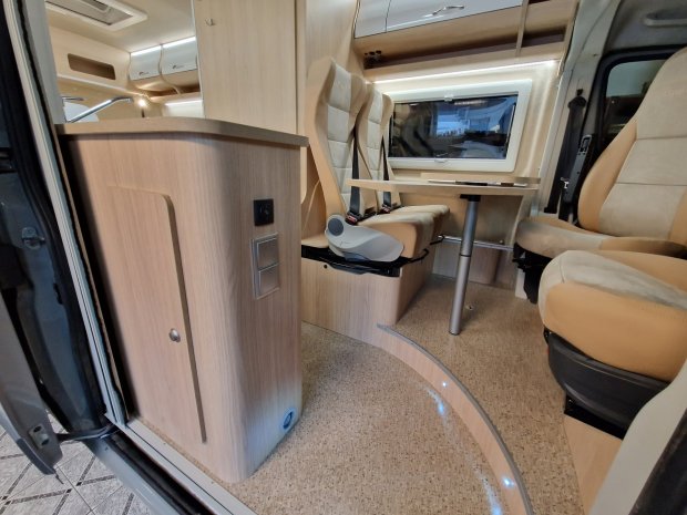 Wnętrze kampera: drewniane meble, stolik i beżowe obrotowe fotele.