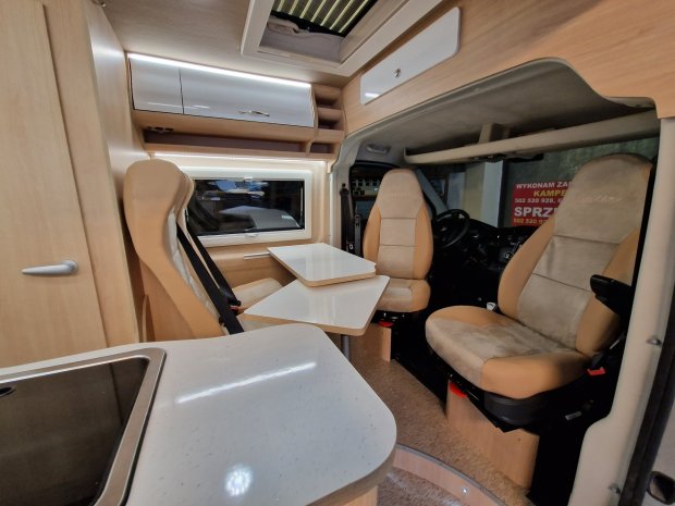 Wnętrze kampera z obrotowymi fotelami, składanym stolikiem i blatem kuchennym