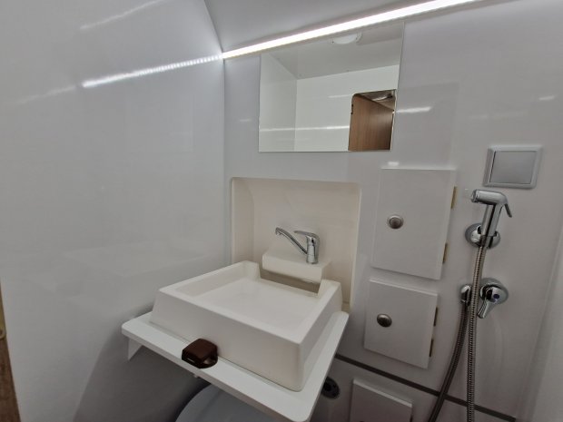 Mała biała umywalka z chromowaną baterią, prysznicem ręcznym i lustrem w kompaktowej łazience