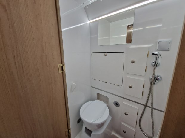Mała biała łazienka w kamperze z toaletą, lusterkiem i prysznicem ręcznym
